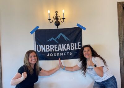 Two women high-five in front of a banner that reads Unbreakable Journeys.